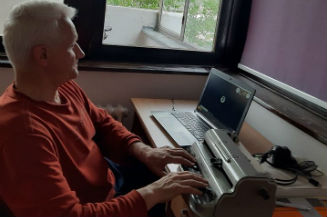 Slika. Udruženje slijepih Kantona Sarajevo realizuje edukaciju za korištenje Iphona. Na slici je Fikret Zuko, direktor Udruženja slijepih Kantona Sarajevo tokom online sastanka prilikom kojeg koristi laptop i Brajevu mašinu.